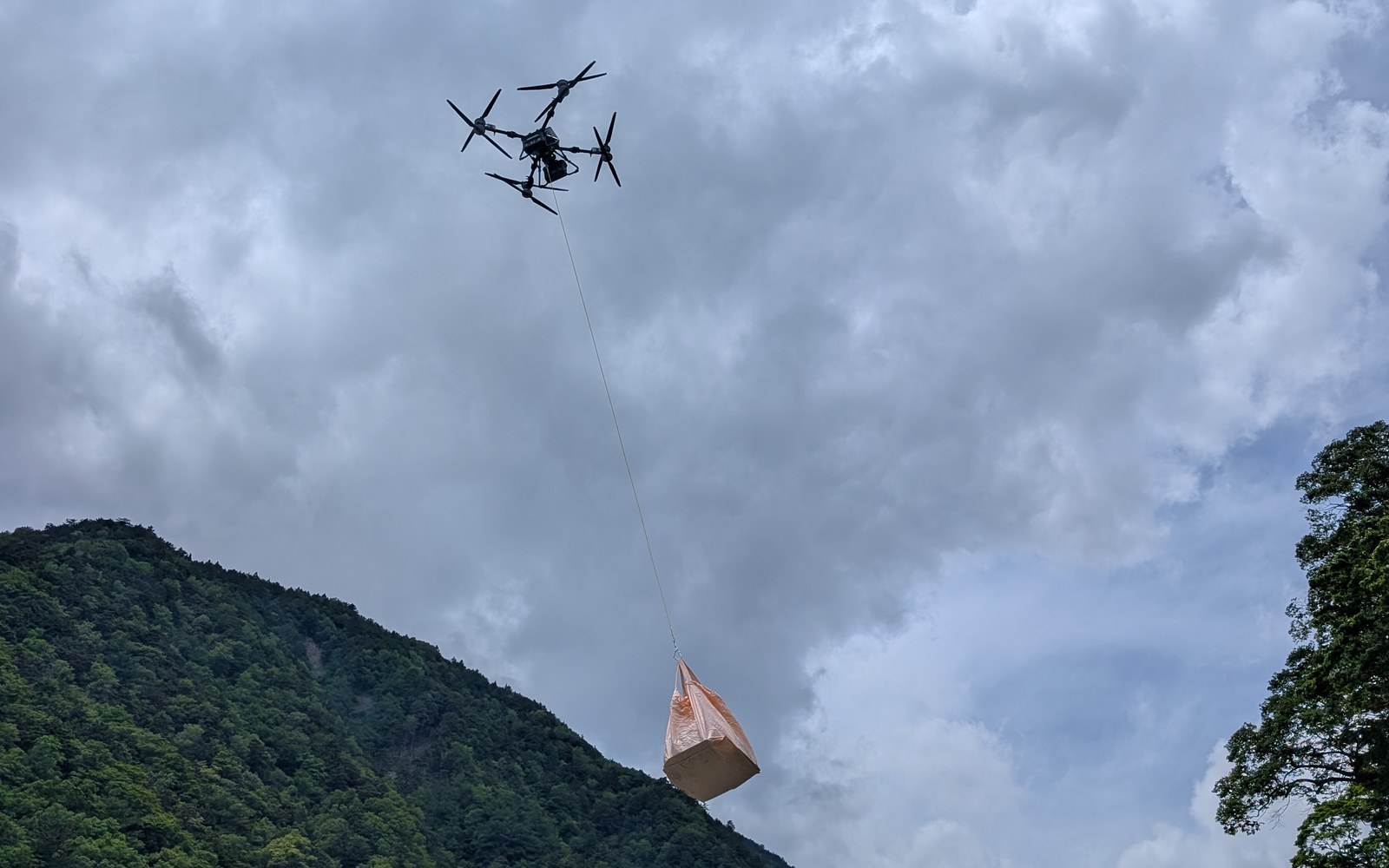 物資の袋をワイヤーで吊り下げ、山の上を飛行するFLYCART 100